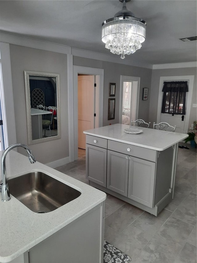 kitchen featuring sink, gray cabinets, light stone counters, ornamental molding, and an island with sink