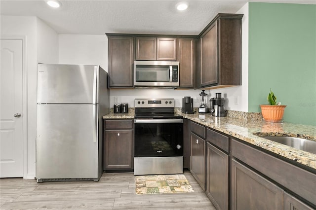 kitchen with stainless steel appliances, light stone countertops, dark brown cabinets, and light hardwood / wood-style flooring