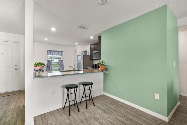 kitchen featuring stainless steel appliances, stone countertops, light hardwood / wood-style floors, and kitchen peninsula