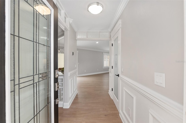 hallway with a wainscoted wall, a decorative wall, crown molding, and wood finished floors