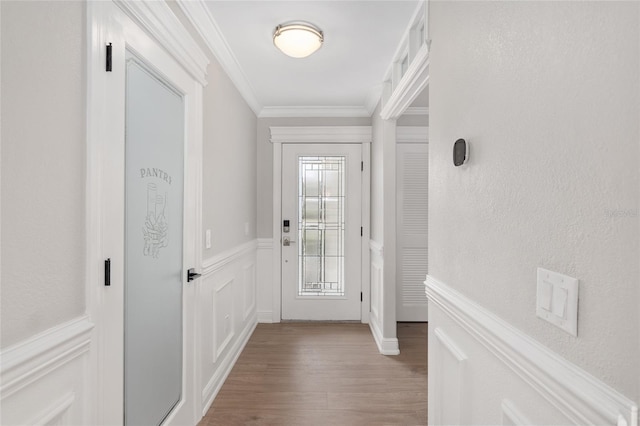 doorway with wainscoting, crown molding, a decorative wall, and wood finished floors