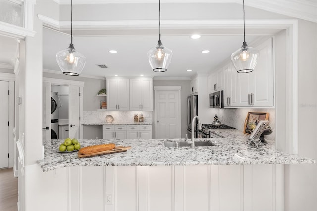 kitchen featuring stacked washer / dryer, white cabinetry, and hanging light fixtures