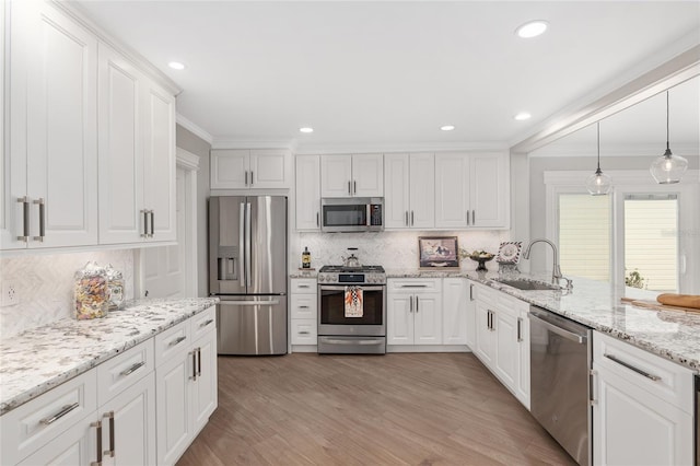 kitchen featuring crown molding, hanging light fixtures, appliances with stainless steel finishes, white cabinetry, and a sink