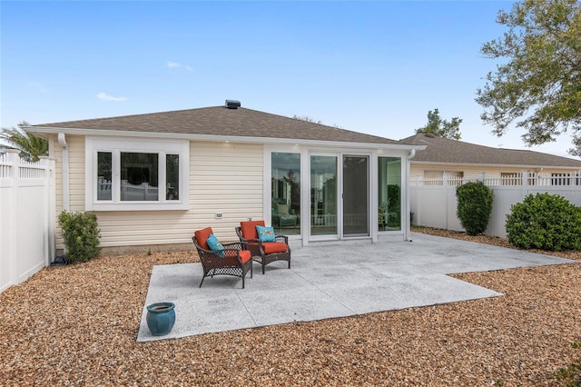 back of property with a shingled roof, a patio area, and a fenced backyard