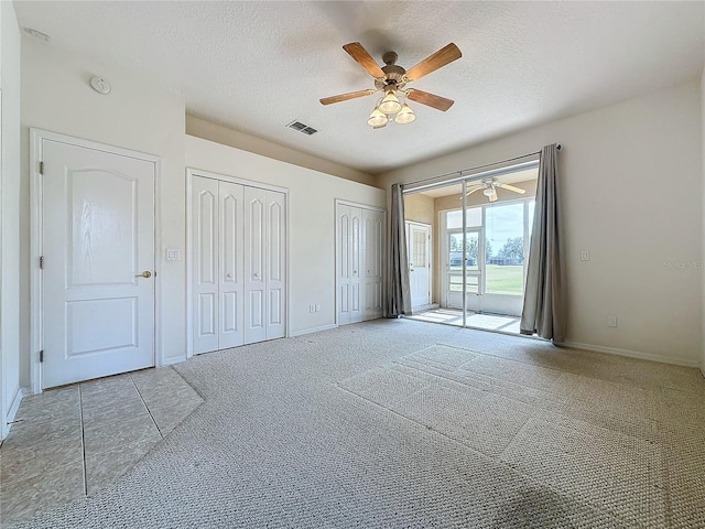 unfurnished bedroom featuring light carpet, access to exterior, a textured ceiling, and multiple closets