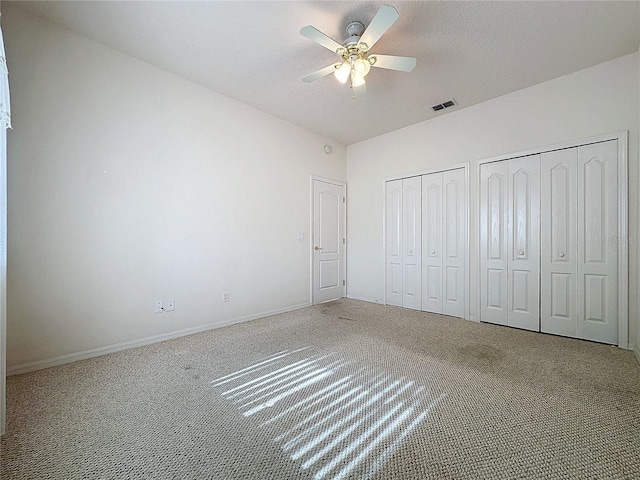 unfurnished bedroom with ceiling fan, a textured ceiling, multiple closets, and carpet flooring