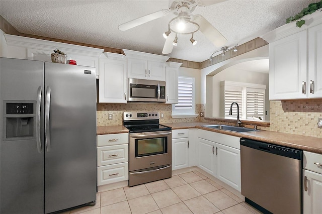 kitchen with stainless steel appliances, sink, light tile patterned floors, and white cabinets