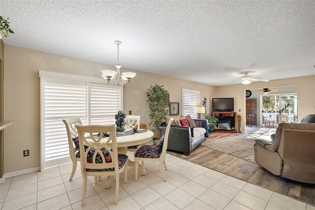dining area with ceiling fan with notable chandelier, light tile patterned floors, and a textured ceiling