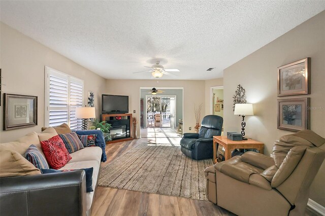 living room featuring ceiling fan, a healthy amount of sunlight, wood-type flooring, and a textured ceiling