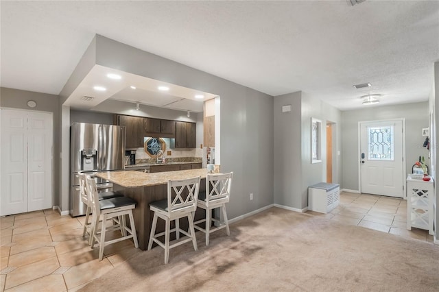 kitchen with a breakfast bar, dark brown cabinetry, a textured ceiling, stainless steel fridge with ice dispenser, and light colored carpet