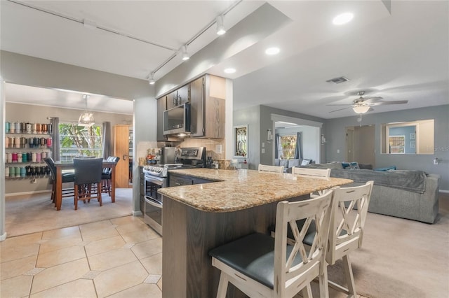 kitchen featuring ceiling fan, appliances with stainless steel finishes, a kitchen breakfast bar, light tile patterned flooring, and kitchen peninsula