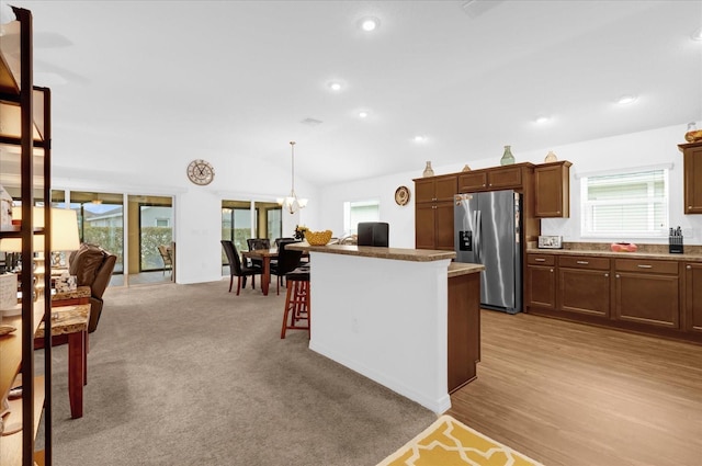 kitchen featuring vaulted ceiling, pendant lighting, a breakfast bar area, stainless steel fridge, and light colored carpet