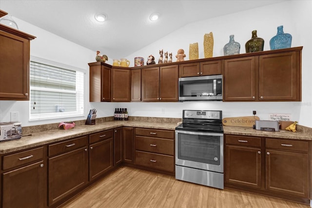 kitchen featuring stainless steel appliances, vaulted ceiling, and light hardwood / wood-style flooring