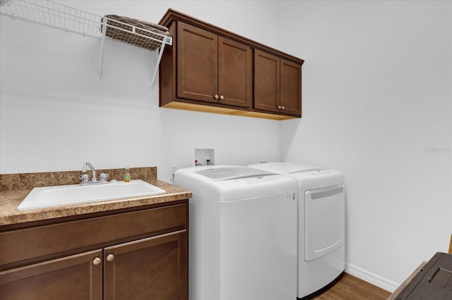 clothes washing area featuring cabinets, washing machine and dryer, hardwood / wood-style flooring, and sink