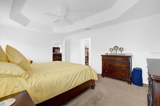 bedroom featuring a walk in closet, light carpet, a raised ceiling, a closet, and ceiling fan