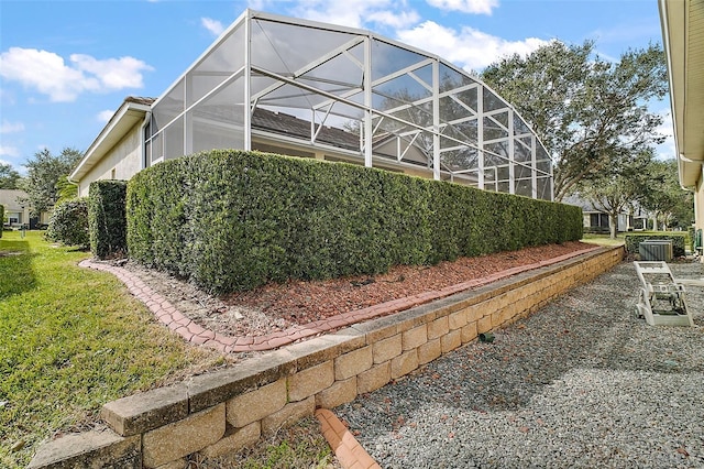 view of side of property featuring a yard, glass enclosure, and central air condition unit