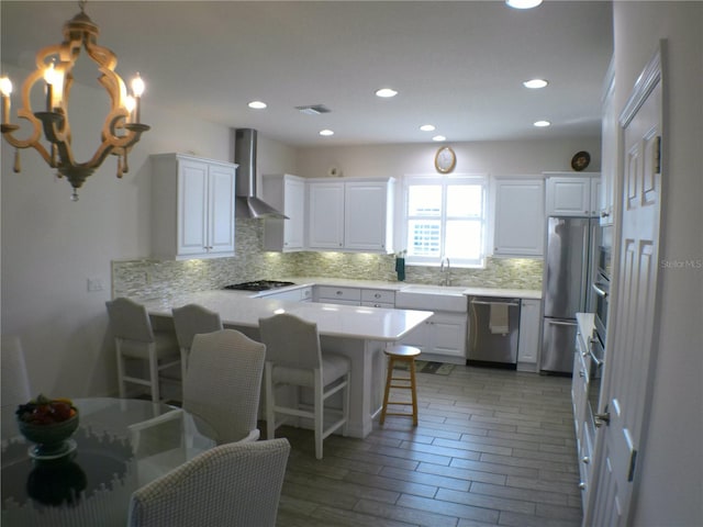 kitchen featuring stainless steel appliances, white cabinetry, a breakfast bar area, and wall chimney range hood