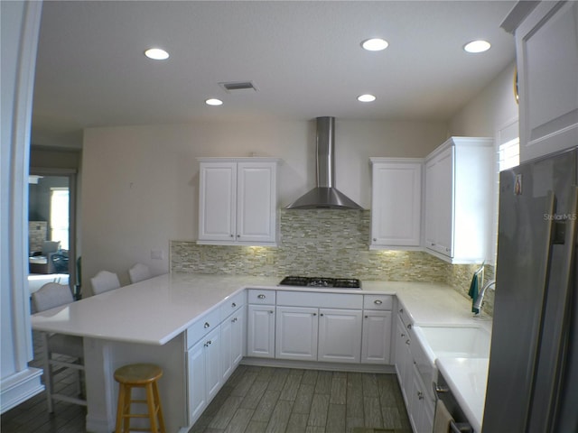 kitchen featuring a breakfast bar area, white cabinets, kitchen peninsula, stainless steel appliances, and wall chimney exhaust hood