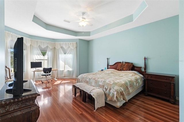 bedroom with hardwood / wood-style flooring, ceiling fan, and a tray ceiling