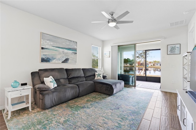 living room featuring a wealth of natural light, ceiling fan, and a water view