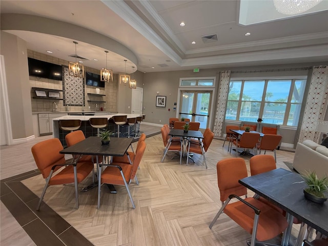 dining space with sink, an inviting chandelier, ornamental molding, a tray ceiling, and light parquet floors