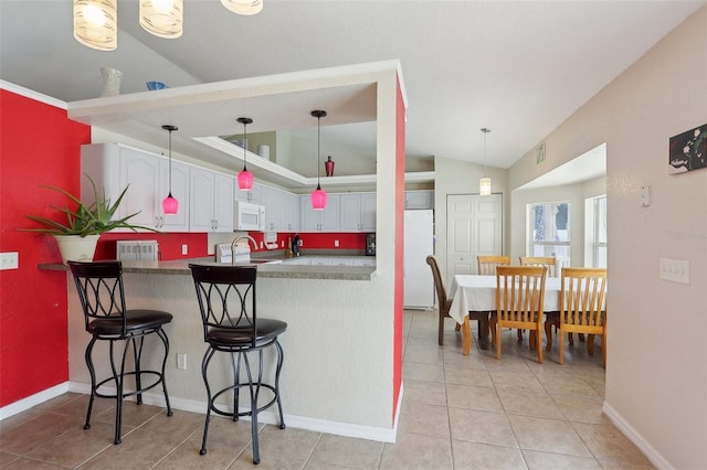 kitchen featuring a peninsula, white appliances, a breakfast bar, white cabinetry, and dark countertops