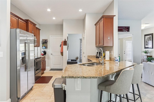 kitchen with sink, a breakfast bar area, appliances with stainless steel finishes, light tile patterned flooring, and kitchen peninsula