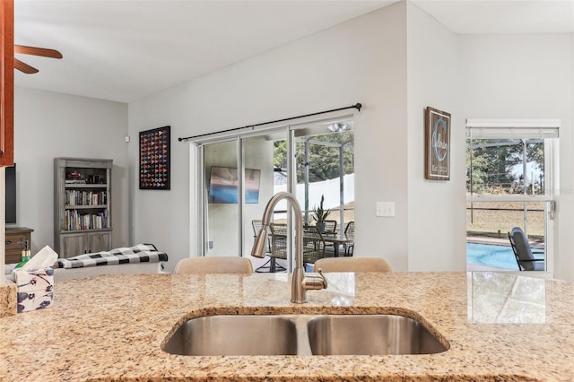 kitchen with light stone counters, ceiling fan, and sink