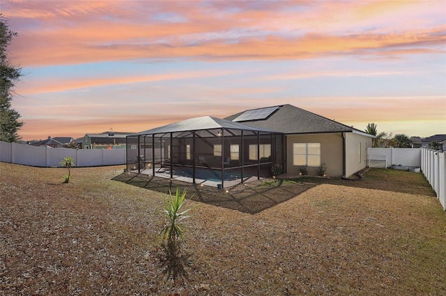 back house at dusk featuring a fenced in pool, a yard, glass enclosure, and solar panels