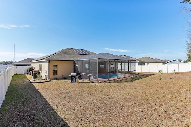 rear view of house with a lanai, a fenced in pool, a lawn, and solar panels