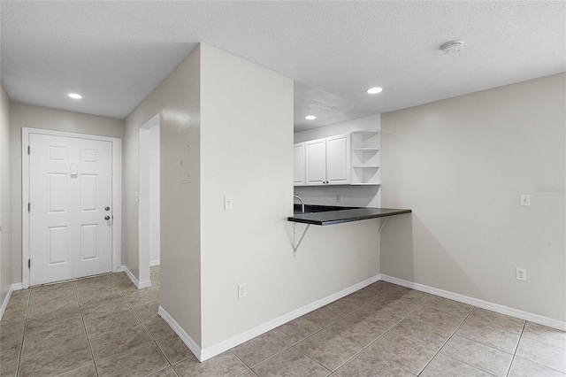 kitchen featuring kitchen peninsula, light tile patterned floors, a textured ceiling, and white cabinets