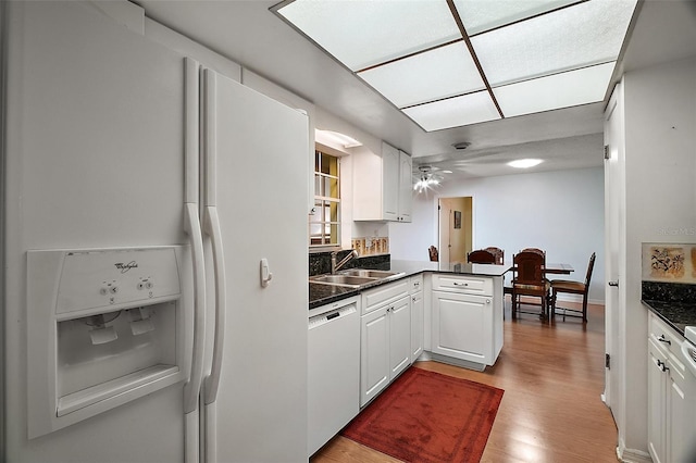 kitchen featuring dark countertops, wood finished floors, a sink, white appliances, and a peninsula