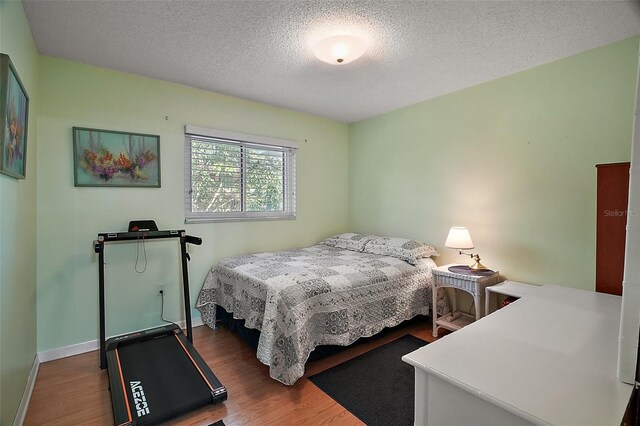bedroom with wood finished floors, a textured ceiling, and baseboards