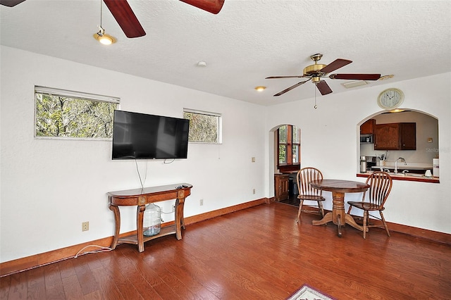 living room with dark wood-type flooring, ceiling fan, and a textured ceiling