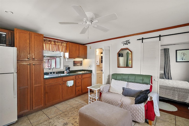 kitchen featuring sink, white refrigerator, light tile patterned floors, ceiling fan, and a barn door