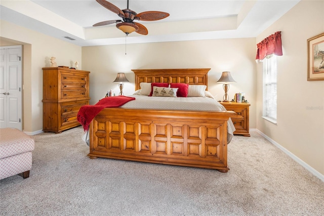 bedroom with light carpet, ceiling fan, and a tray ceiling