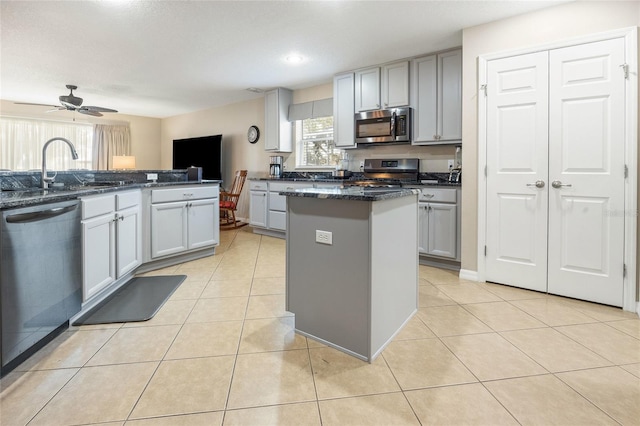 kitchen with stainless steel appliances, light tile patterned flooring, a center island, and dark stone counters