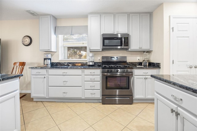 kitchen with dark stone countertops, stainless steel appliances, white cabinets, and light tile patterned flooring