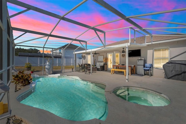 view of pool with an in ground hot tub, a patio, ceiling fan, and glass enclosure