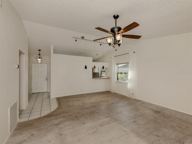 unfurnished living room featuring ceiling fan, lofted ceiling, light hardwood / wood-style floors, and a textured ceiling