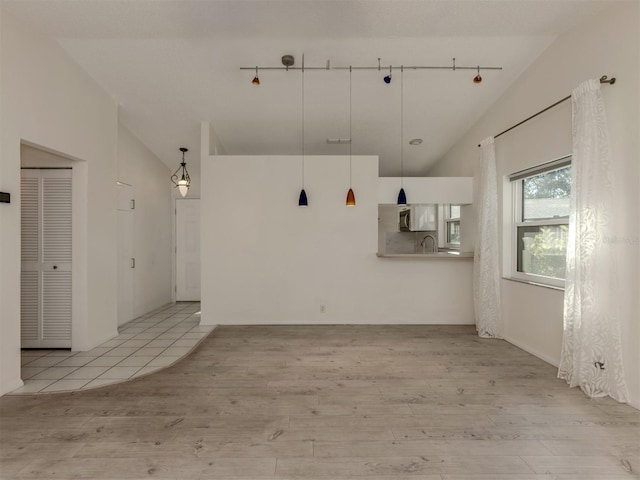 spare room with lofted ceiling, sink, track lighting, and light hardwood / wood-style floors