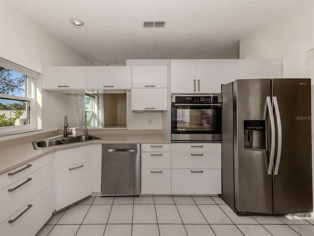 kitchen with light tile patterned flooring, sink, white cabinets, stainless steel appliances, and a textured ceiling