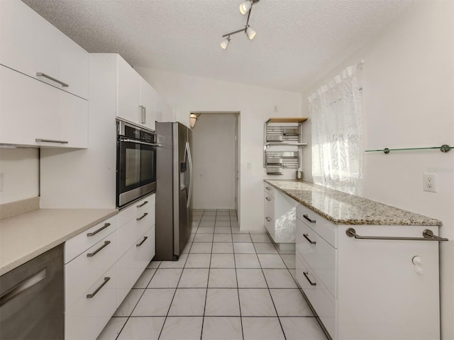 kitchen with white cabinets, light tile patterned floors, stainless steel appliances, light stone countertops, and a textured ceiling