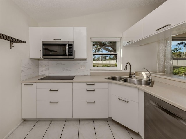 kitchen featuring sink, dishwashing machine, white cabinets, black electric stovetop, and backsplash