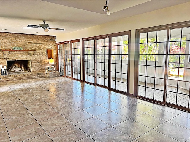 unfurnished living room featuring a brick fireplace, tile patterned floors, ceiling fan, and brick wall