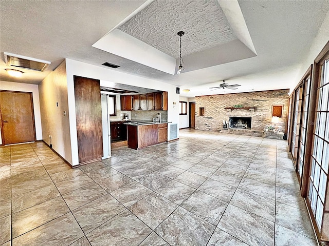 kitchen featuring hanging light fixtures, a textured ceiling, a raised ceiling, ceiling fan, and a fireplace