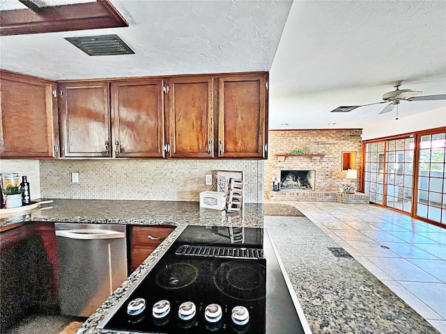 kitchen featuring ceiling fan, dark stone countertops, a fireplace, a textured ceiling, and decorative backsplash