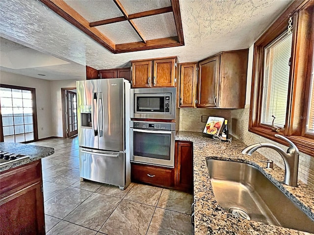 kitchen featuring sink, backsplash, light stone counters, stainless steel appliances, and a textured ceiling