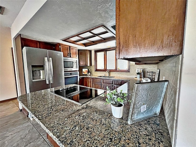 kitchen featuring sink, dark stone countertops, kitchen peninsula, stainless steel appliances, and backsplash