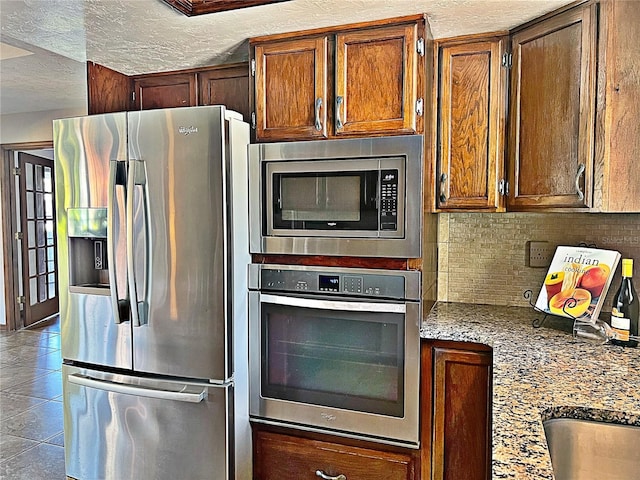 kitchen featuring light tile patterned floors, stainless steel appliances, light stone counters, a textured ceiling, and decorative backsplash